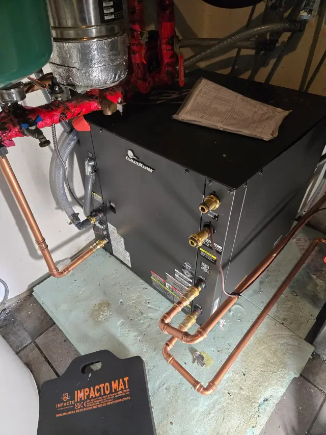 ClimateMaster unit with red insulated pipes, black box, and copper tubing