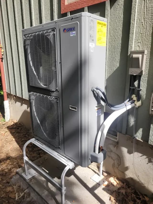 A large outdoor heat pump unit with a fan, branded 'Gree', is installed on a stand. It's a