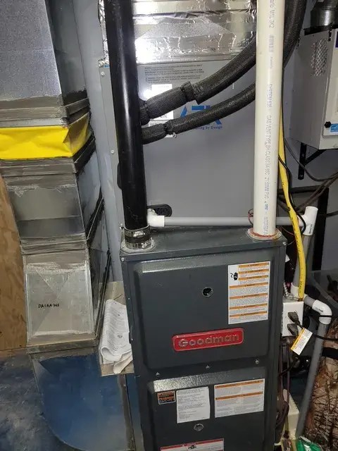 Goodman furnace with black and red casing, surrounded by various equipment and wiring