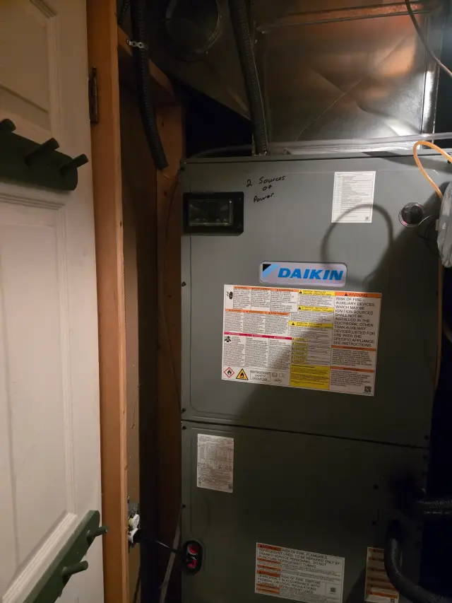 Image of a Daikin furnace with two power sources connected, showing the back panel with various labels and