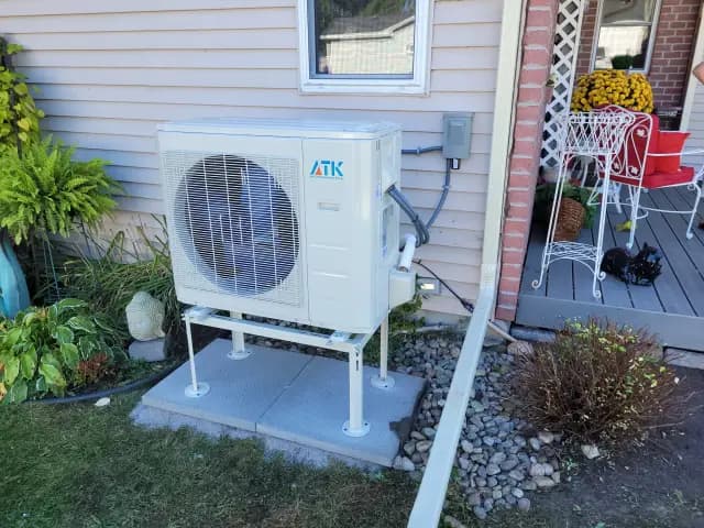 A large white outdoor heat pump with the brand 'Gree' visible is installed on a concrete platform next