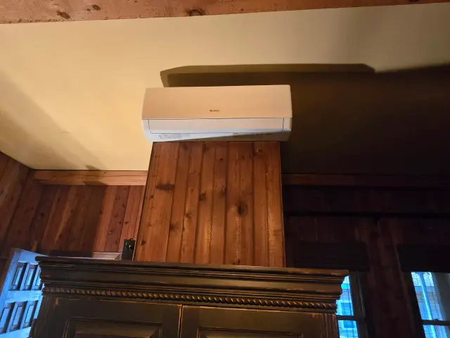 Air conditioning unit with a white casing is mounted on a wooden wall