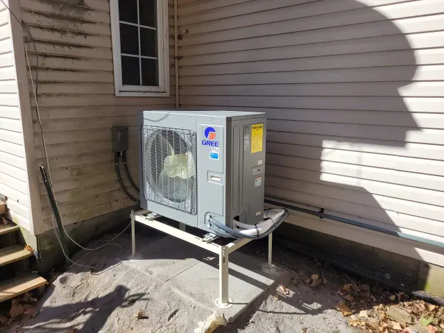 A newly installed outdoor Gree heat pump with a large fan and a gray casing is placed on