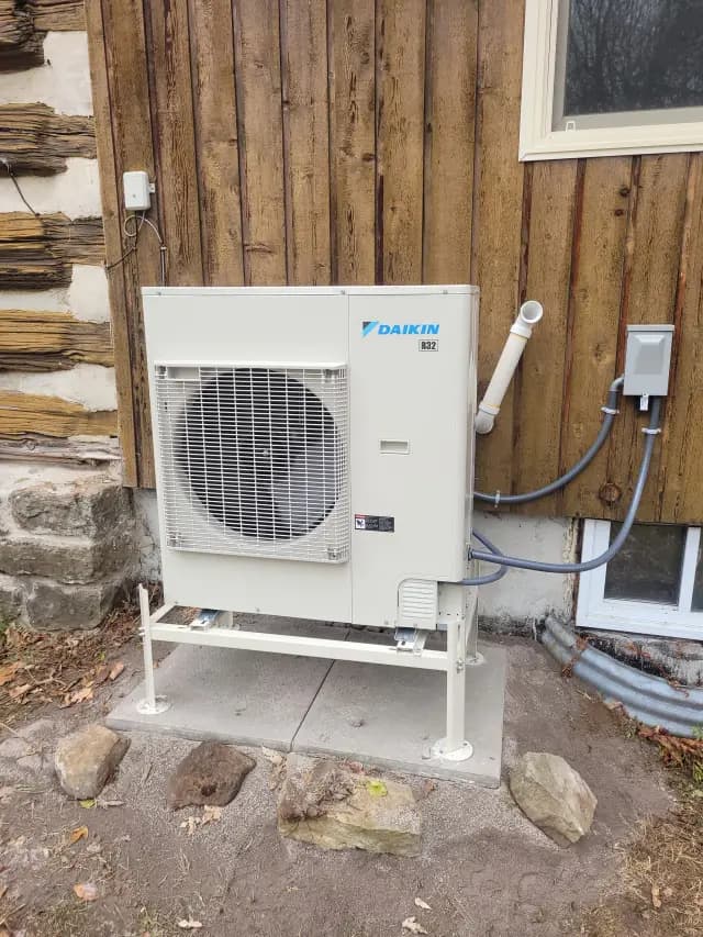 Outdoor heat pump installed near a wooden house wall