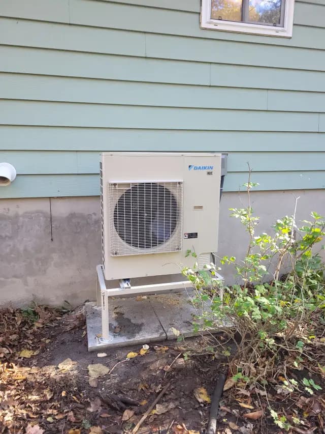 Outdoor heat pump unit with Daikin logo, installed on a stand with a large fan in front