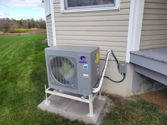 A newly installed outdoor Gree heat pump with a large fan and a gray casing is placed on
