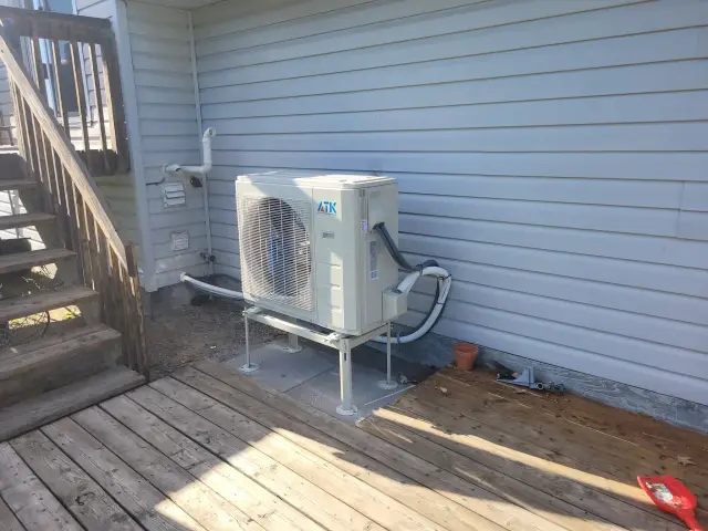 A new outdoor heat pump unit is installed on the side of a house, with a large fan