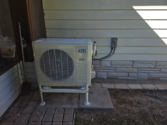 A new outdoor heat pump unit, branded with the Gree logo, is installed on a concrete platform outside