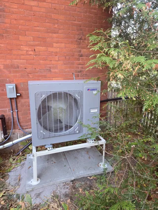 A large outdoor unit with a fan and a Gree logo is installed against a brick wall. There