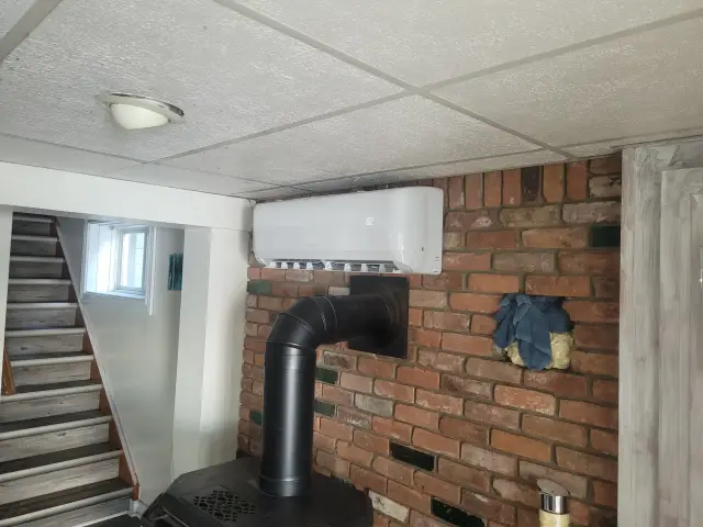 A white Gree heat pump is installed outside, with a black vent tube extending upwards into the sky.