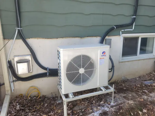 A new Gree heat pump is installed outside a house, with a large fan visible and black wiring