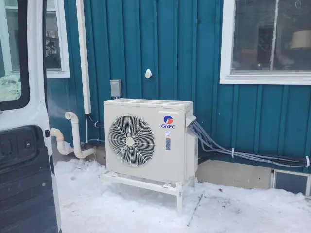 A Gree heat pump unit is installed outside a building. It's a white, rectangular unit with a large