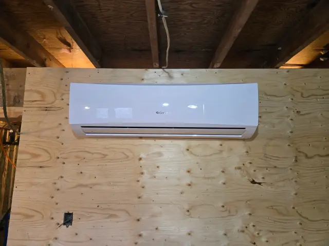 Outdoor Gree heat pump installed on wooden wall with exposed rafters above