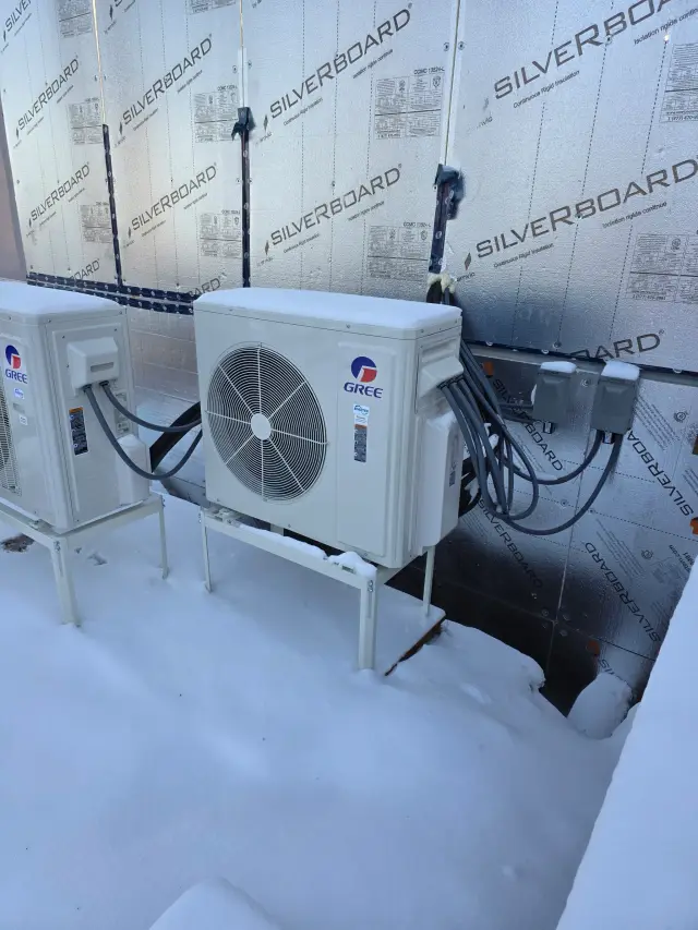 A Gree heat pump unit is installed outdoors on a snowy day, with a clear view of its