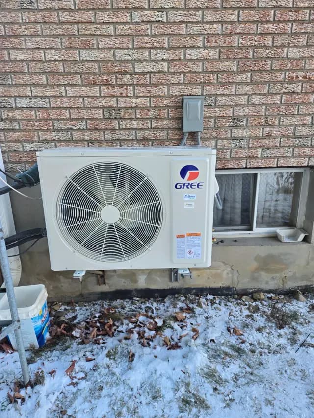 A large outdoor unit with a circular fan is mounted on the side of a brick house. The