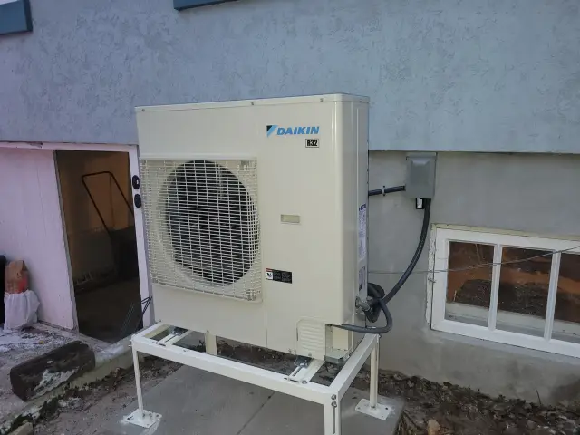 A Daikin heat pump unit is installed outside a house, with a large fan visible on the front.