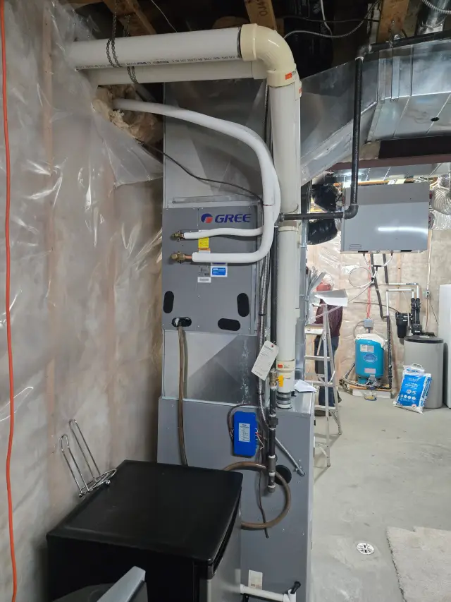 Outdoor Gree heat pump with white piping and control box, installed on concrete foundation