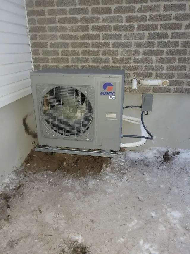 A large outdoor unit with a fan, branded with the Gree logo, is installed against a brick wall