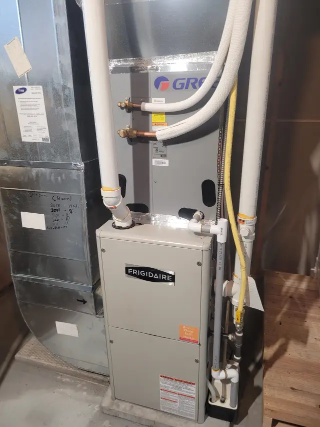 Outdoor Gree heat pump installed on concrete foundation with metal siding. Two white pipes connected to the unit