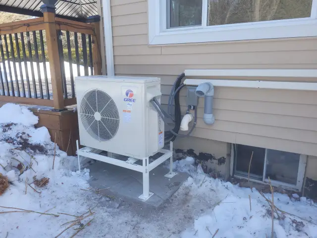 A new Gree heat pump is installed outside a house, with snow on the ground around it