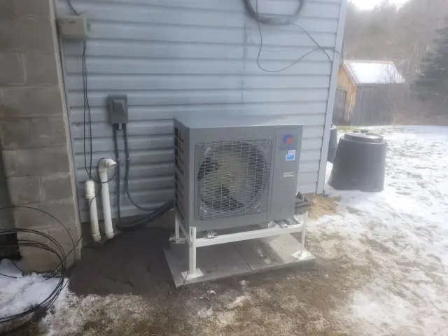 Outdoor heat pump installed near house with snow on the ground