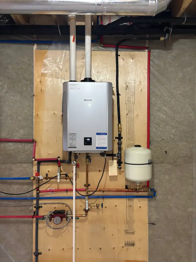 A Rinnai tankless water heater is mounted on a wooden board with various pipes and fittings attached to