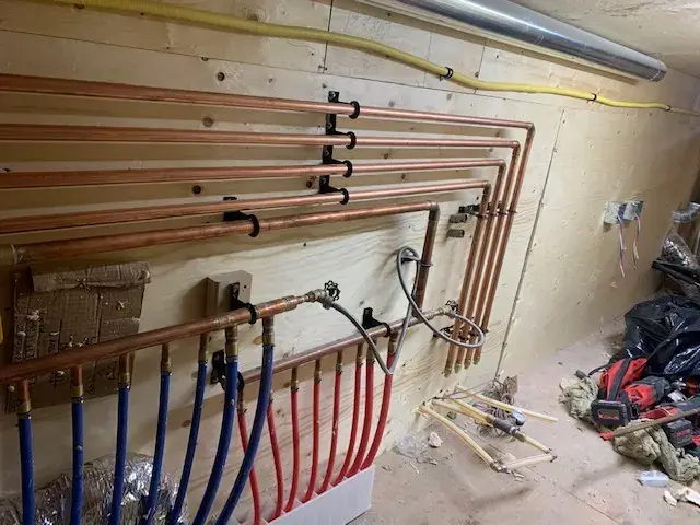 Copper pipes are neatly arranged on a wooden wall with various fittings and connections. The pipes are organized