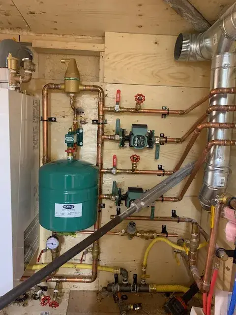 Copper pipes with valves and an expansion tank are neatly installed on a wooden wall