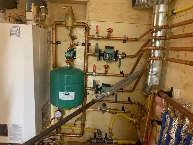 Copper pipes with green expansion tank, valves, and fittings installed on wooden wall
