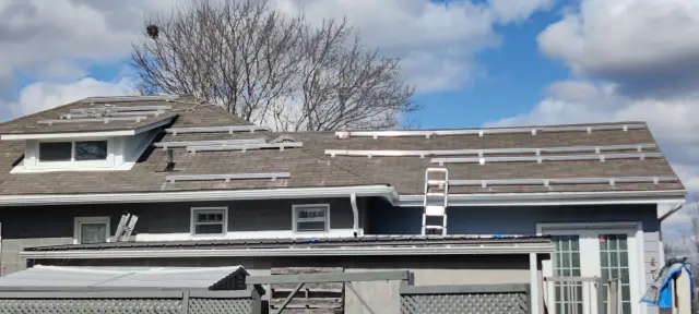 Solar panels on a residential roof with a ladder leaning against the house