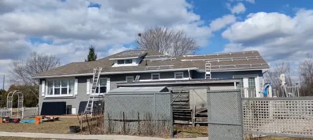 Solar panels on a house roof with a ladder leaning against the house