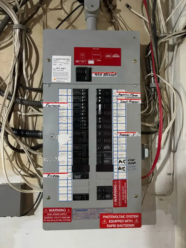 An electrical panel with numerous switches and breakers, surrounded by various wires and cables, with labels