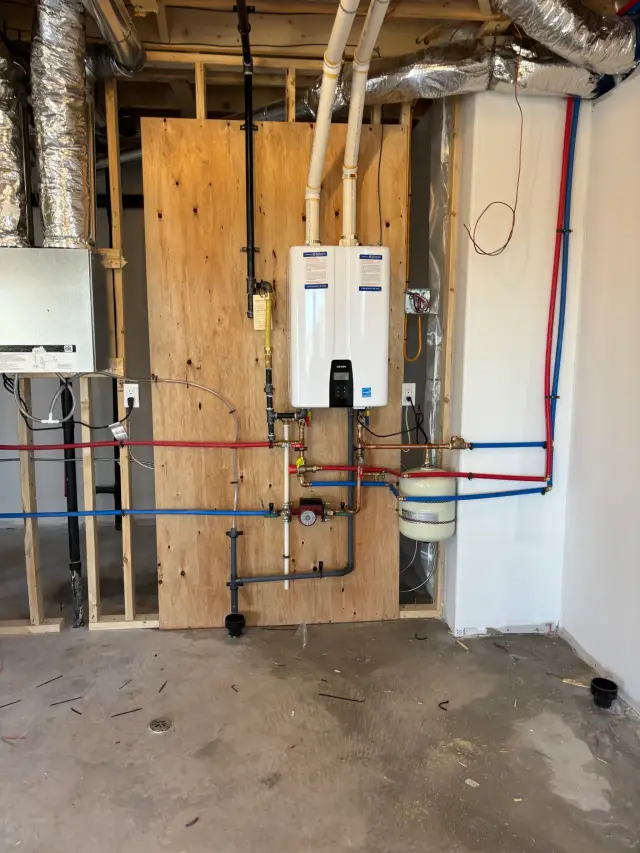 Image of HVAC ductwork with silver insulation wrapped around pipes, attached to wooden wall with various plumbing