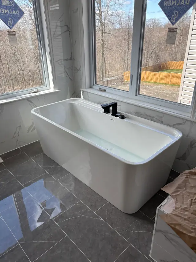A white freestanding bathtub with a black faucet is positioned against a backdrop of marble walls. The tub