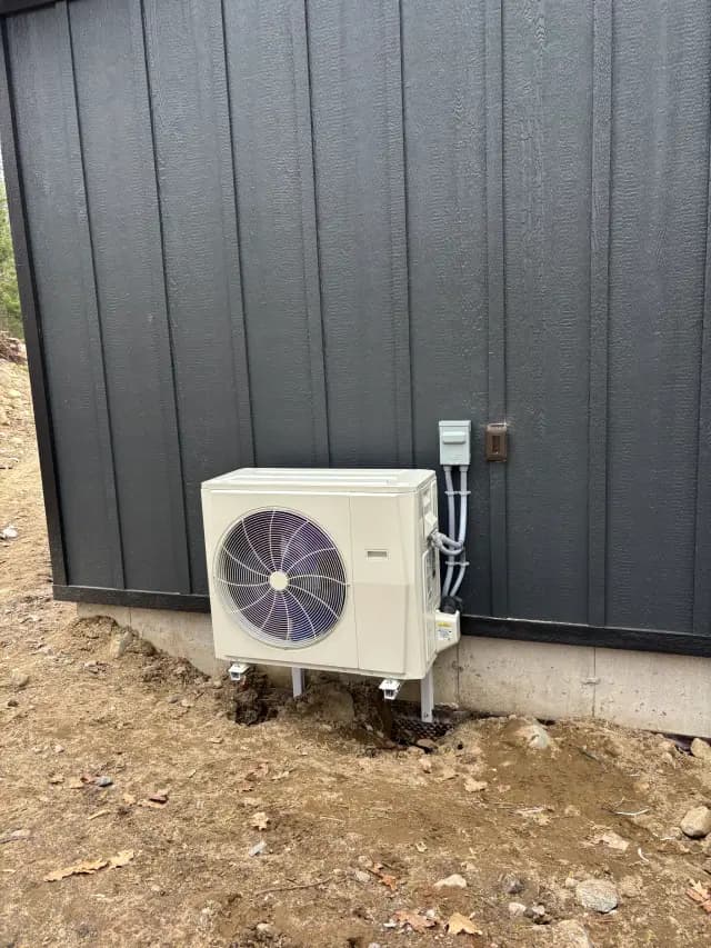 An outdoor Gree heat pump with a large fan is installed against a black wall. It is surrounded