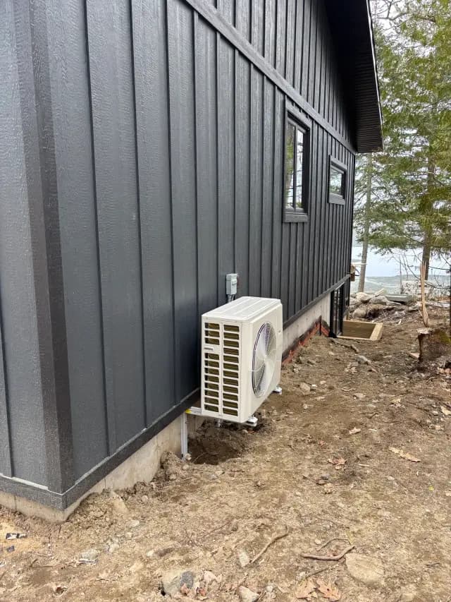 A white Gree heat pump is installed outside a house with a black exterior. The pump is on