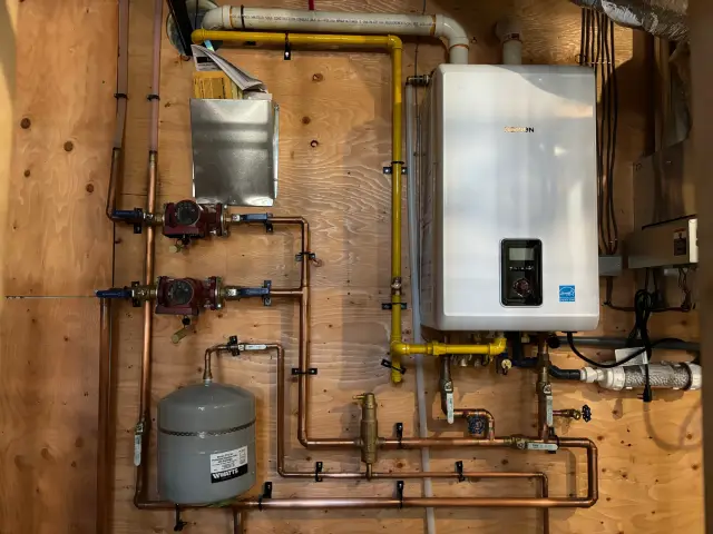 Tankless water heater with digital display and yellow piping installed on wooden wall with various pipes and fittings