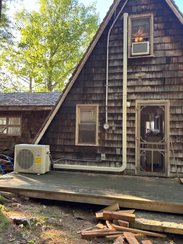 A Gree heat pump is installed outside a house, with a white casing and a blue hose connected
