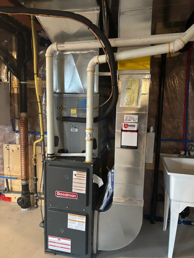 Goodman furnace with its control panel and piping installed in a room with insulation and other utilities