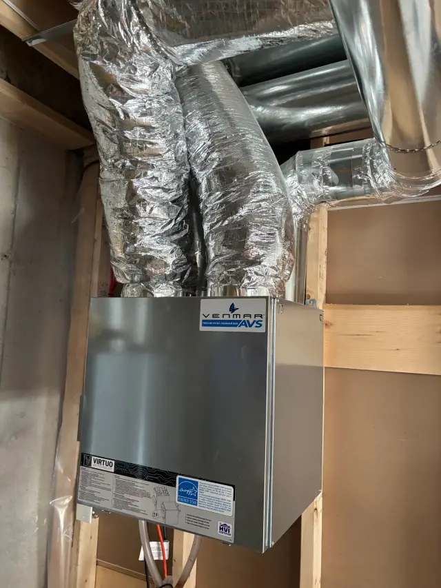 Outdoor Gree heat pump with silver metallic casing and blue logo, installed on wooden platform with clear sky