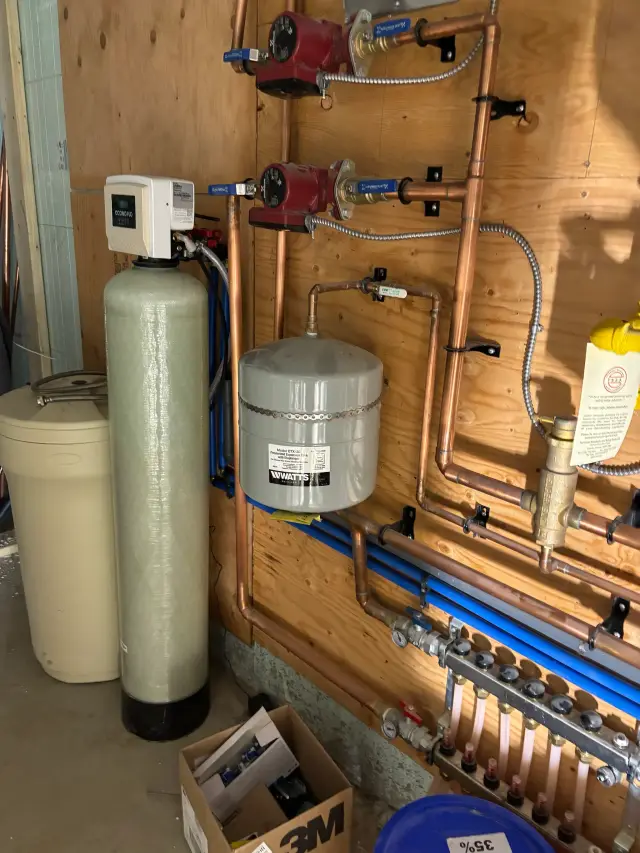 A large, cylindrical water softener tank with a white exterior and a black base is mounted on a