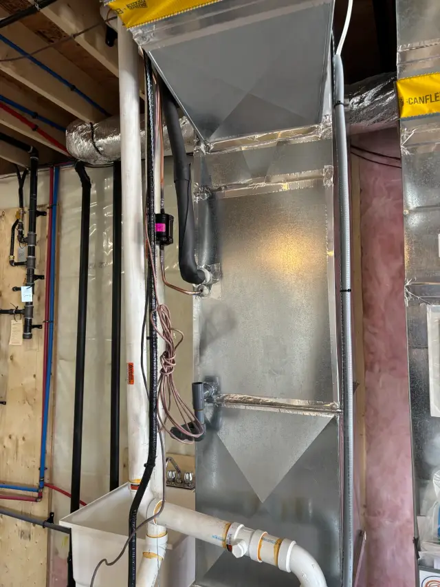 Canflex ducting is installed on the wall, with various pipes and wires running alongside. The ducting is silver,