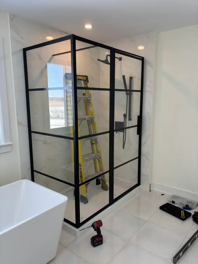 A shower enclosure with black frame and clear glass panels is under construction. The glass is not yet