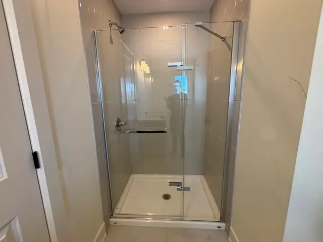 A clear glass shower enclosure with a silver frame is installed in a bathroom with beige walls and
