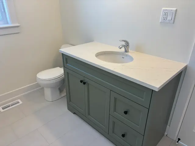 A bathroom sink with a silver faucet is set into a white countertop, with a green cabinet below