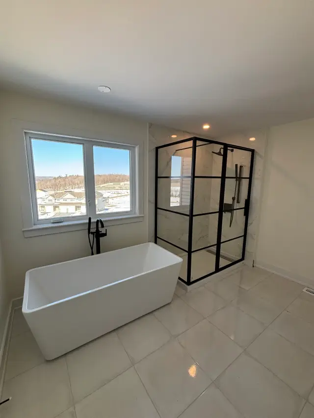 A spacious bathroom features a white freestanding tub with a contemporary faucet, next to a glass-enclosed shower with