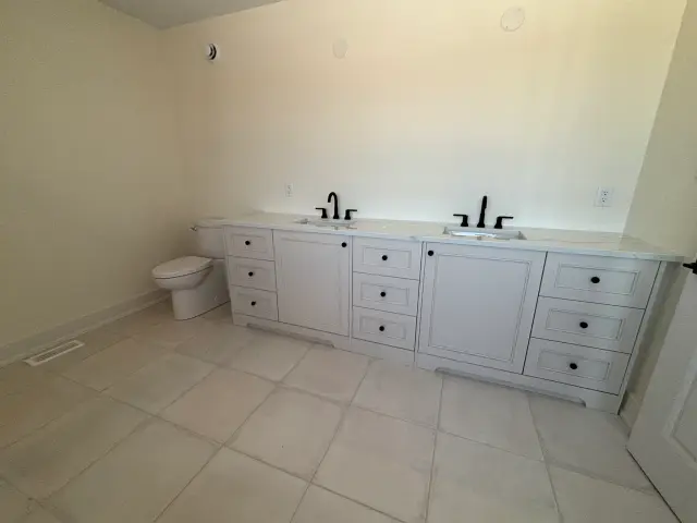 A spacious bathroom features a long, white vanity with two sinks, each equipped with a modern, black faucet.