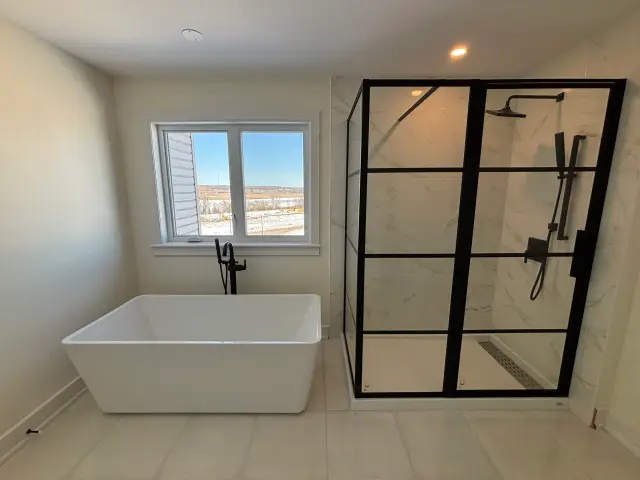 A white freestanding bathtub with a contemporary black faucet is positioned next to a window overlooking a snowy