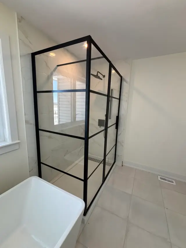 A spacious bathroom showcases a sleek glass shower enclosure with a black frame, complemented by a white bathtub