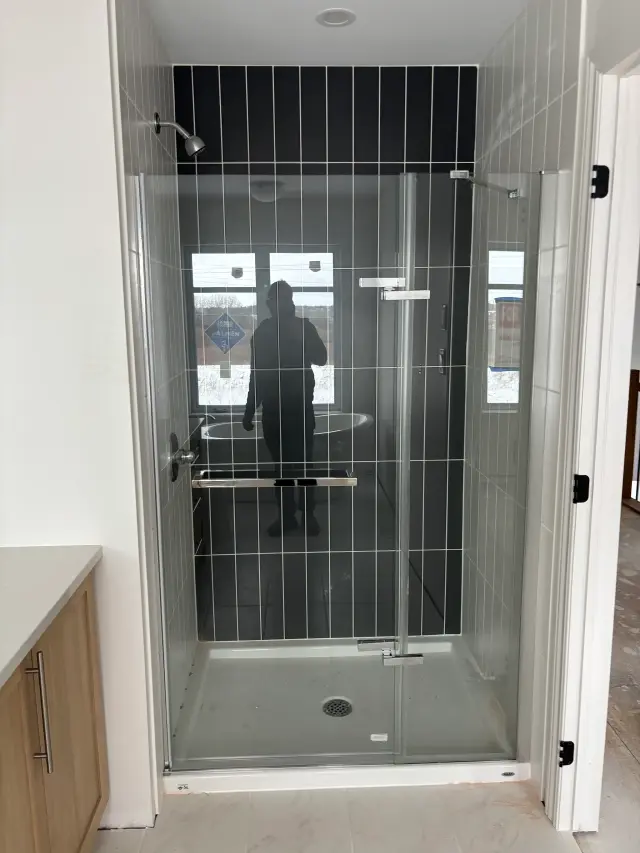 A modern shower stall with black tiles and clear glass doors is installed in a bathroom. The shower